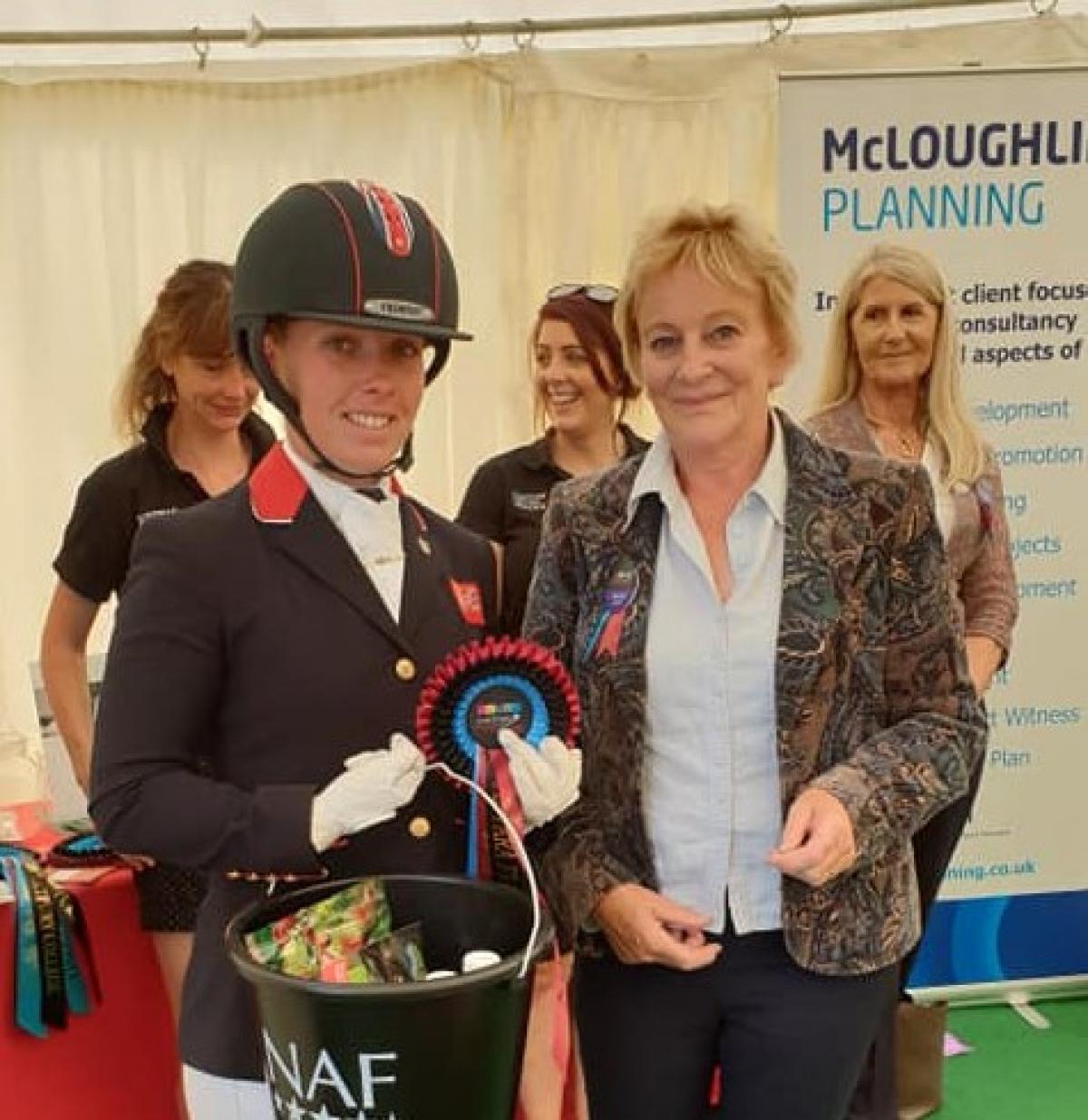 Sophie Wells - Great Britain - equestrian British female dressage athlete holds bucket of prize with an organiser