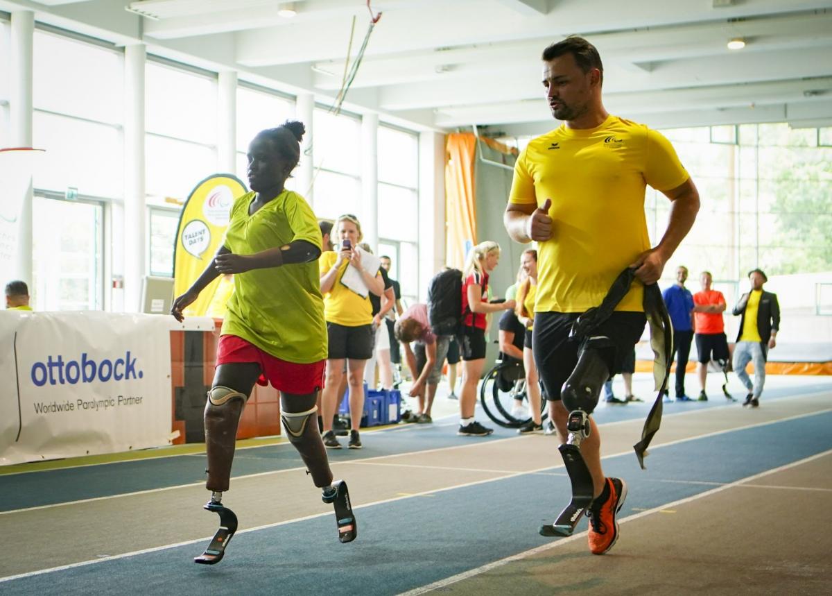 Male sprinter with prothesis runs alongside a young double-amputee sprinter girl