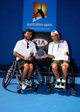 A picture of 2 men in a wheelchair holding a cup