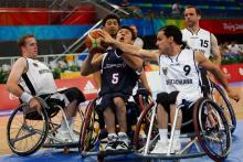 A picture of a man in a wheelchair trying to shoot a ball betwenn other men in wheelchair