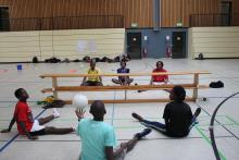 A picture of 6 young people sit down and playing Sitting Volleyball