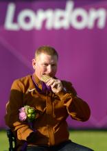 A picture of a man in a wheelchair showing his gold medal.