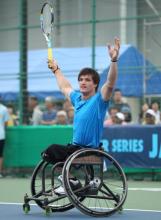 A picture of a man in a wheelchair wearing a tennis racket and celebrating his victory