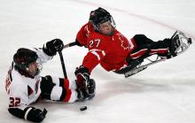 A picture of a 2 men in a sldege playing hockey