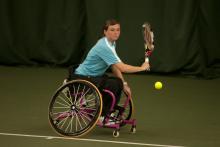 A picture of a young woman in a wheelchair playing a backhand during a wheelchair tennis match.