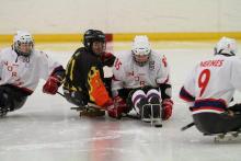 A picture of four men in sledges playing ice hockey.