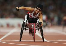 A picture of a woman in the wheelchair on a track celebrating the victory with her hand up