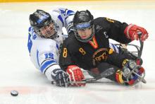 A picture of two men in sledge fighting the puck during a ice hockey match