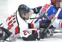 A picture of two men in sledges playing ice hockey