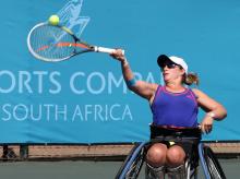 A picture of a woman in a wheelchair playing a forehand during a wheelchair tennis game