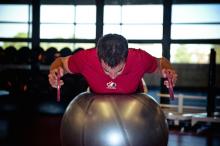 An athlete lies on a stability ball holding weights with both hands close to him.