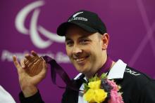 Portrait of smiling man wearing a basecap showing his bronze medal to the camera.