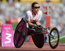 A female wheelchair racer leans forward in her chair wearing sunglasses