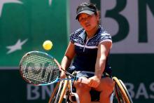 Woman in wheelchair on a tennis court returning a shot.