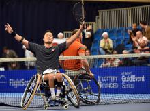 Man in wheelchair, holding tennis racket in triumphing pose