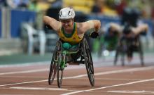 a female from Australia competing in a wheelchair with green and yellow clothes and a white helmet